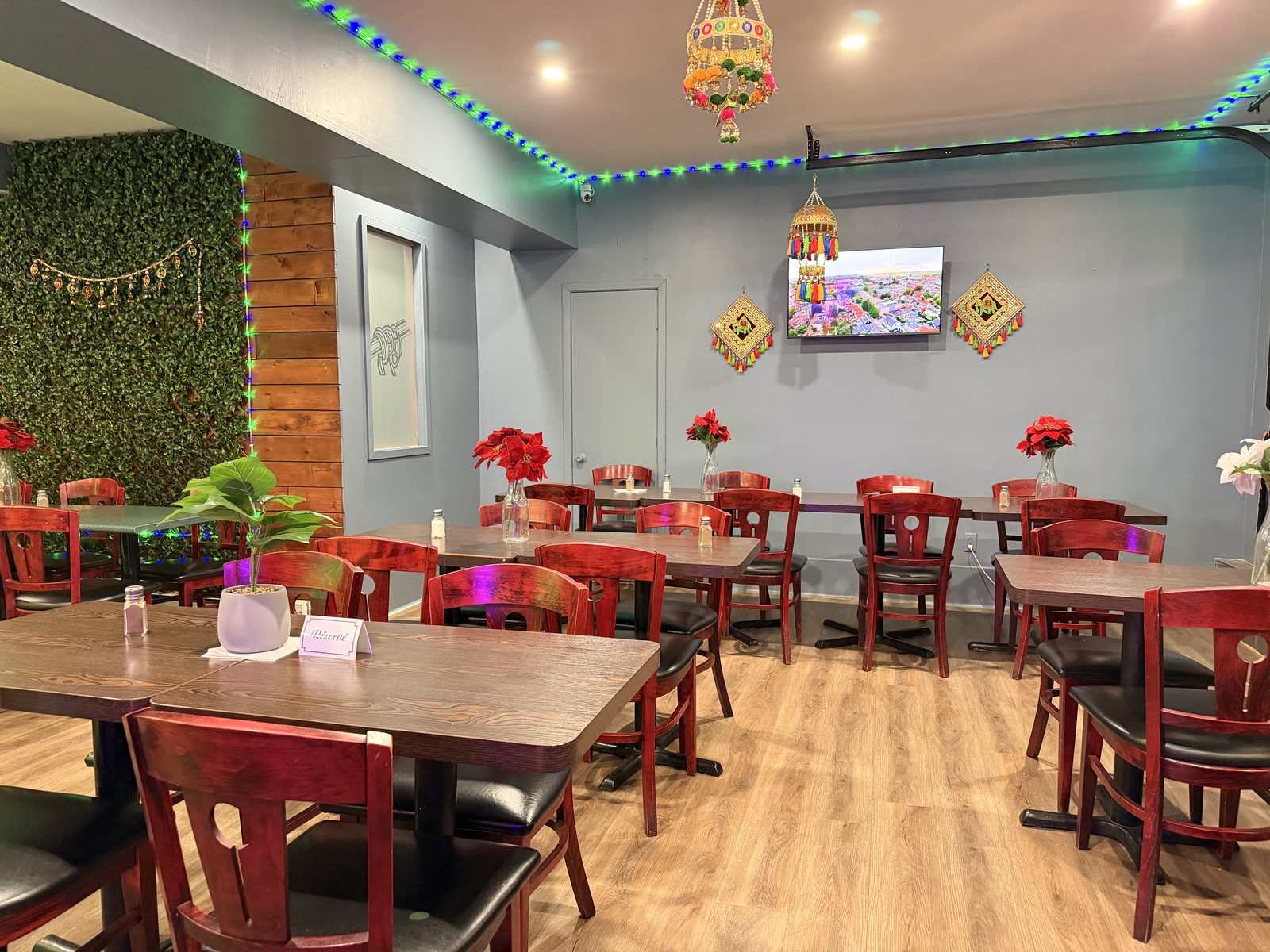 The dining room at Restaurant Indian Spices — warm wood tables, red chairs, fresh flowers and festive lights